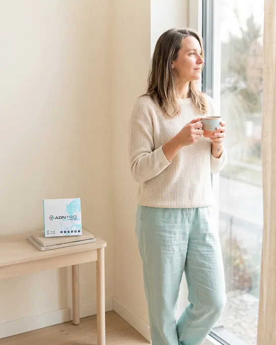 Woman with a cup by her living room window, with the ADNTRO saliva kit on the side table